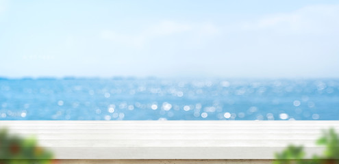Aufkleber - Empty white plank wood table with blur blue sky and sea bokeh background with green leaf foreground,Mock up template for display or montage of product or content use as banner in social media ads