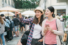 Asian Girl Friends At Farmer Market Outdoors In Summer In City. Two Young Female Travelers Holding Cellphone With Map Online App Searching And Point Finger While Find Shop Destination Tokyo Japan