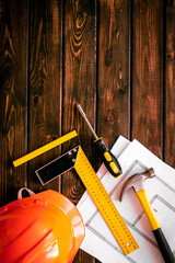 Builder work desk with hard hat, instruments and blueprints on dark wooden background top-down frame copy space