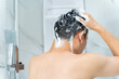 © twinsterphoto - Back view from below of black haired naked man washing hair with shampoo while talking shower in bathroom