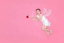 Happy Smiling Baby Cupid In Costume Angel Wings, Bow And Heart Arrow Isolated On Pink Studio Background. Copyspace For Text. Valentines Day Concept.