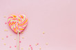  Big striped heart-shaped lollipop and confectionery confetti on a pink background copy space. Background for Valentine's Day in pink, yellow and orange colors. 