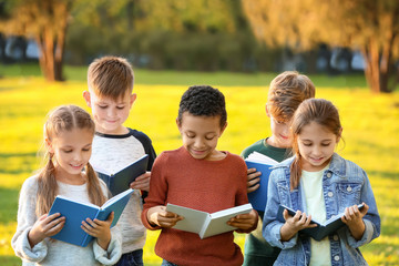 Cute little children reading books in park