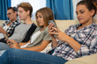 © carles - Girl looking at a mobile next to a group of people using the mobile on a sofa
