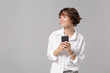 © ViDi Studio - Smiling young business woman in white shirt posing isolated on grey wall background studio portrait. Achievement career wealth business concept. Mock up copy space. Hold mobile phone, looking aside.