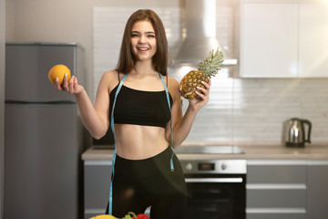 young fit woman with centimeter round neck wearing black top and black leggings with pineapple in one hand and orange in another dietology and nutrition