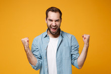 Joyful Young Bearded Man In Casual Blue Shirt Posing Isolated On Yellow Orange Wall Background, Studio Portrait. People Sincere Emotions Lifestyle Concept. Mock Up Copy Space. Doing Winner Gesture.
