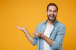 © ViDi Studio - Laughing young bearded man in casual blue shirt posing isolated on yellow orange wall background, studio portrait. People sincere emotions lifestyle concept. Mock up copy space. Pointing hands aside.