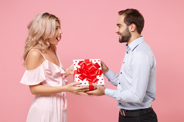 Shocked young couple two guy girl in party outfit celebrating posing isolated on pastel pink background. Valentine's Day Women's Day birthday holiday concept. Hold present box with gift ribbon bow.