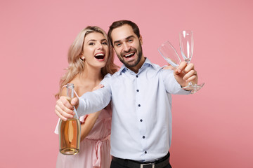 Joyful young couple two guy girl in party outfit celebrating posing isolated on pastel pink background. Valentine's Day Women's Day birthday holiday party concept. Holding glass bottle of champagne.