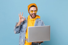 Funny Young Hipster Guy In Fashion Jeans Denim Clothes Posing Isolated On Pastel Blue Wall Background. People Lifestyle Concept. Mock Up Copy Space. Working On Laptop Pc Computer, Showing OK Gesture.