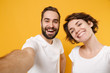 © ViDi Studio - Close up of cheerful young couple friends bearded guy girl in white t-shirts isolated on yellow orange wall background. People lifestyle concept. Mock up copy space. Doing selfie shot on mobile phone.