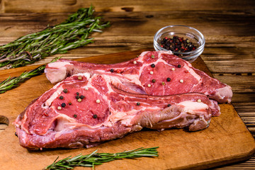 Raw ribeye steak, glass jar with spices and rosemary on cutting board