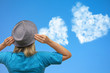 Girl in hat looks at clouds in heart shape soar in blue sky. Concept of love, romance and happy relations. Valentine day or wedding greeting card. Pure clear skyline with emotional expression