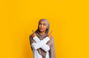 Wall Mural - Doubtful black muslim girl pointing at copy space with crossed hands