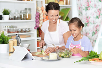 Cute little girl with her mother cooking together at kitchen table