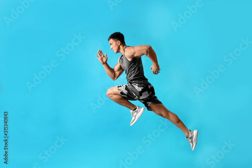 Fotomural Athletic young man running on light blue background, side view