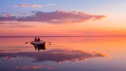a couple in love look at beautiful sunset in a rowing boat on the lake. pink sky and vanilla clouds.