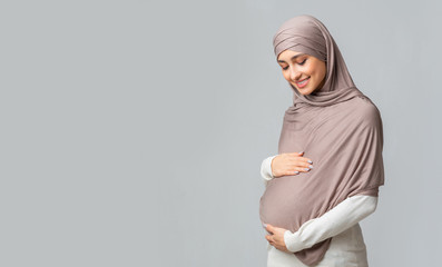 Canvas Print - Pregnant muslim woman embracing her belly, posing over grey background