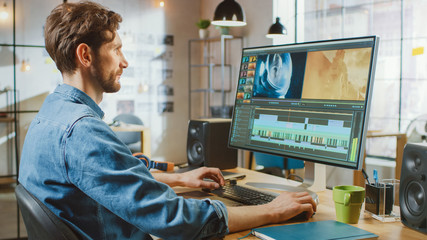 Wall Mural - Beautiful Creative Male Video Editor with Beard and Jeans Shirt Works with Footage on His Personal Computer with Big Display. He Works in a Cool Bright Office Loft.