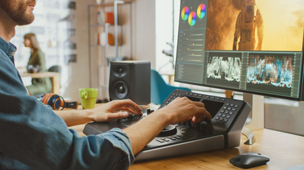 Wall Mural - male video editor with beard and jeans shirt works with footage on his computer using an editing con
