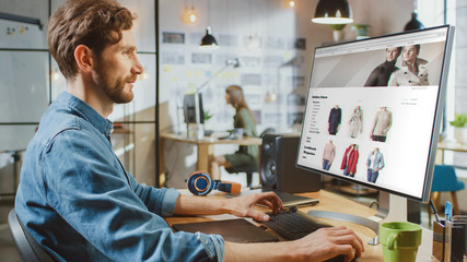 Wall Mural - beautiful male scrolls through online fashion store on his personal computer with big display. he wo