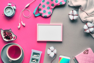 Healthy night sleep creative concept. Sleeping mask, alarm clock, earphones, earplugs, tea and pills. Split two tone pink and green background with natural cotton textile and flowers, copy-space.