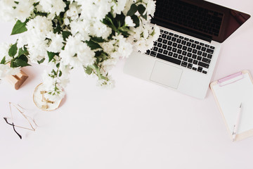 Wall Mural - Office desk workspace with laptop, flowers bouquet and clipboard on pink table. Flat lat, top view freelancer co-working background.