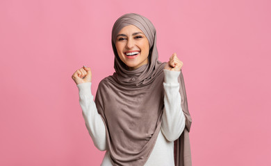 Wall Mural - Excited middle-eastern woman celebrating success, raising hands and clenching fists