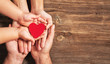 © Sondem - family hands holding red heart on wooden background. Donation, charity, health concept.