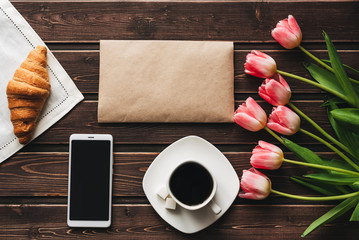 Wall Mural - Cup of coffee with a croissant for Breakfast on the table decorated with a bouquet of pink tulips and a smartphone