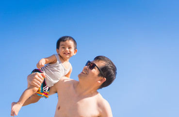 Wall Mural - Asian father is playing and holding his happy little baby boy on the backgroud of blue sky in summer vacation time, concept of love relation and outdoor activity for kid and parent in family lifestyle