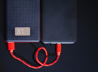 Smartphone charging with black Power Bank through USB cable on black background