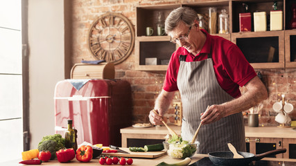 Wall Mural - Caring grandfather preparing salad at home kitchen