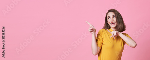 Photographie Beautiful healthy young woman smiling with his finger pointing and looking at on light pink banner background with copy space