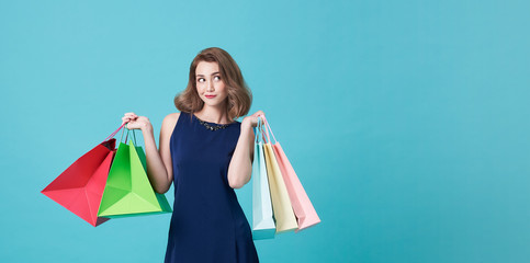 Happy beautiful young woman in blue dress and hand holding shopping bags and looking at on light blue banner background with copy space.