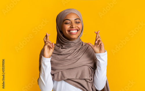 Positive afro muslim woman in hijab making wish with crossed fingers Tableau sur Toile