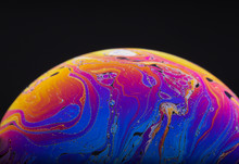 Close Up Macro Photograph Of The Psychedelic Rainbow Of Colors Mixing And Swirling In A Soap Bubble To Look Like A Fantasy Galaxy Or Planet Isolated Against A Black Background