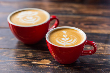 Two red cups of coffee on wooden background with latte art. Table in cafe. Concept of easy breakfast. Small and big ceramic cups