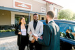 © sofiko14 - Young Caucasian man car dealer explaining sales contract to couple in business wear, african man and caucasian woman, buying a car, standing outdoors in auto salon