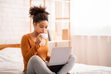 Woman Using Laptop Having Coffee Sitting On Bed In Bedroom