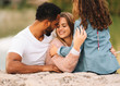 © Gabriel Trujillo/ADDICTIVE STOCK - Happy casual multiracial parents lying on sandy ground together and looking with admiration at content daughter sitting beside and embracing father