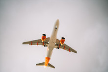 From Below Of White And Orange Aircraft Flying With Cloudy Grey Sky On Background