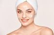 © Indico Studio/ADDICTIVE STOCK - Positive freckled woman with towel on head and healthy skin taking care of face with cream and looking at camera isolated on white background