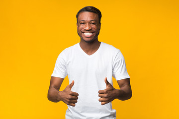 Wall Mural - Afro Man Gesturing Thumbs-Up Posing Over Yellow Studio Background