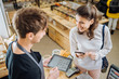 © Iryna - Small business, people, takeaway and service concept. Happy man owner stands behind counter giving paper bag to female customer at zero waste bakery grocery shop.