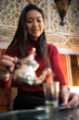 © Juan Alberto Ruiz/ADDICTIVE STOCK - Happy ethnic female pouring fresh Arabic tea in cup while sitting on comfortable couch in small ornamental room