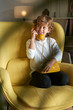 © PHILIPPE DEGROOTE/ADDICTIVE STOCK - Little boy in white t shirt and jeans sitting on yellow comfortable armchair and talking on fusty telephone and looking away