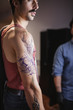 © Raquel Arocena/ADDICTIVE STOCK - Side view of crop serious male checking details of tattoo template on arm carefully while standing with master in workshop