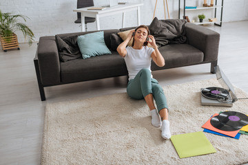 Wall Mural - dreamy girl listening music in headphones near sofa and vintage record player